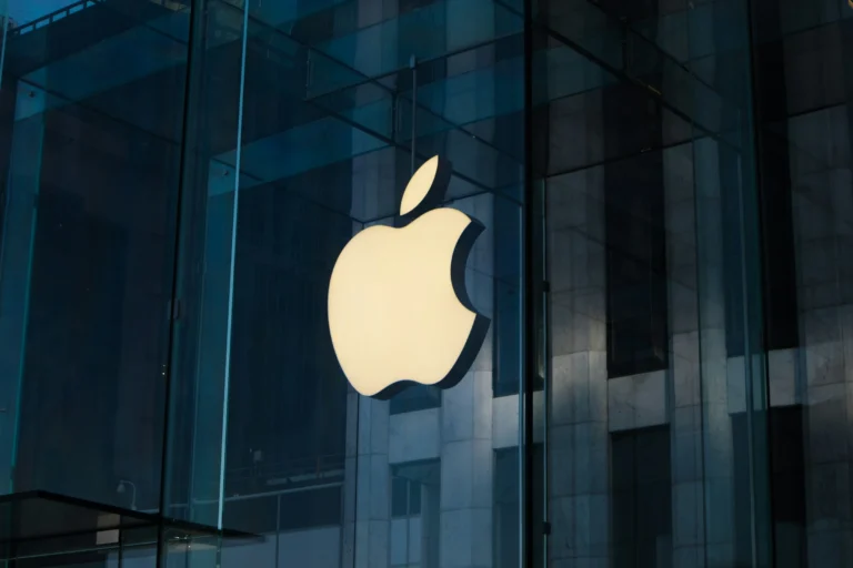 Apple logo glowing outside a modern glass building, symbolizing innovation